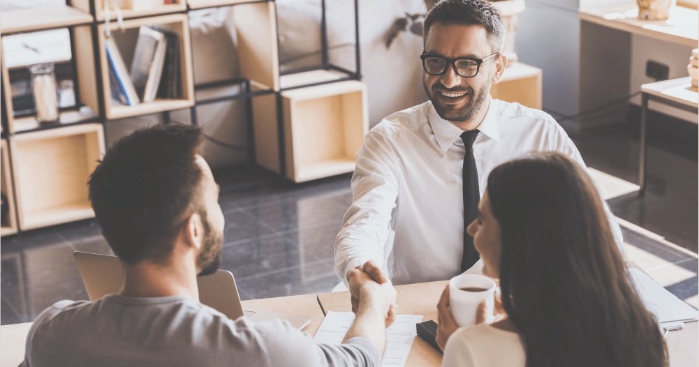 Casal cumprimenta um gerente sorridente em uma mesa de atendimento
