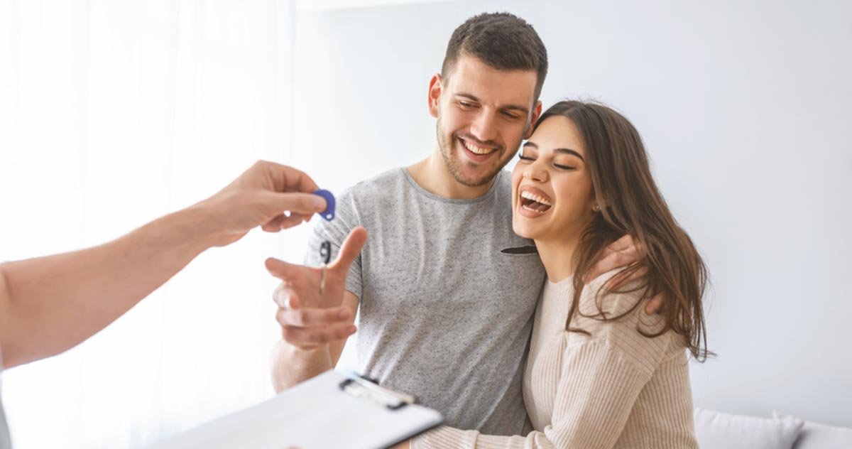 Casal abraçado e sorridente recebe as chaves do novo imóvel