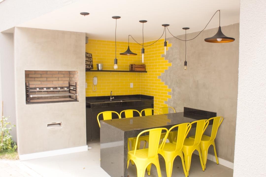 Foto do espaço gourmet com churrasqueira, bancada e banquetas amarelas