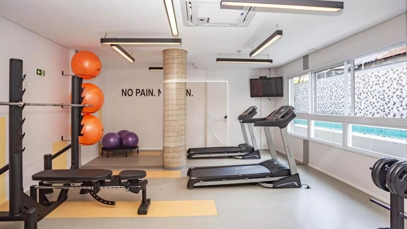Foto da academia entregue, com esteiras, banco de musculação e bolas de pilates