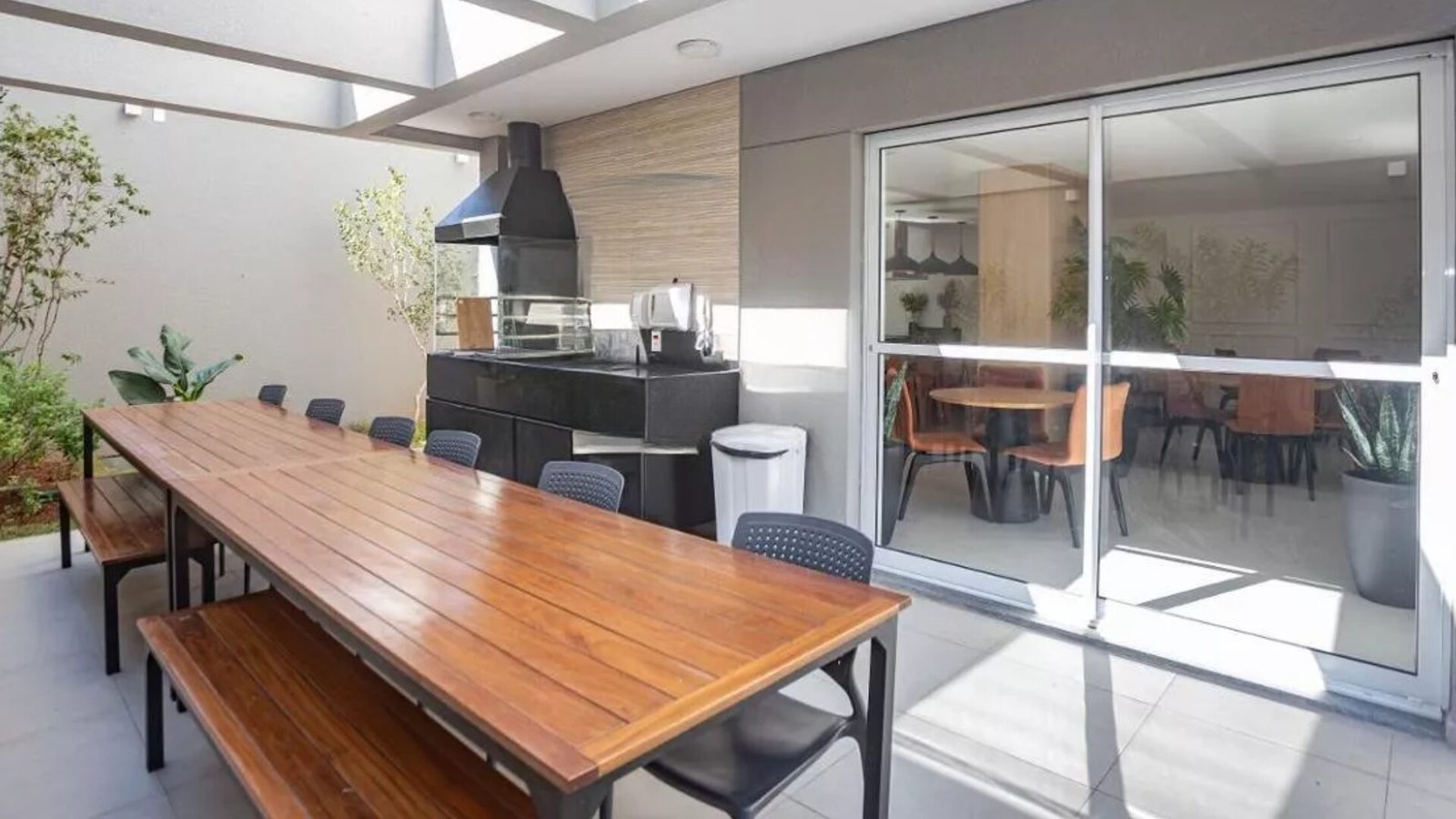 Foto da churrasqueira com mesa comprida de madeira e acesso ao salão