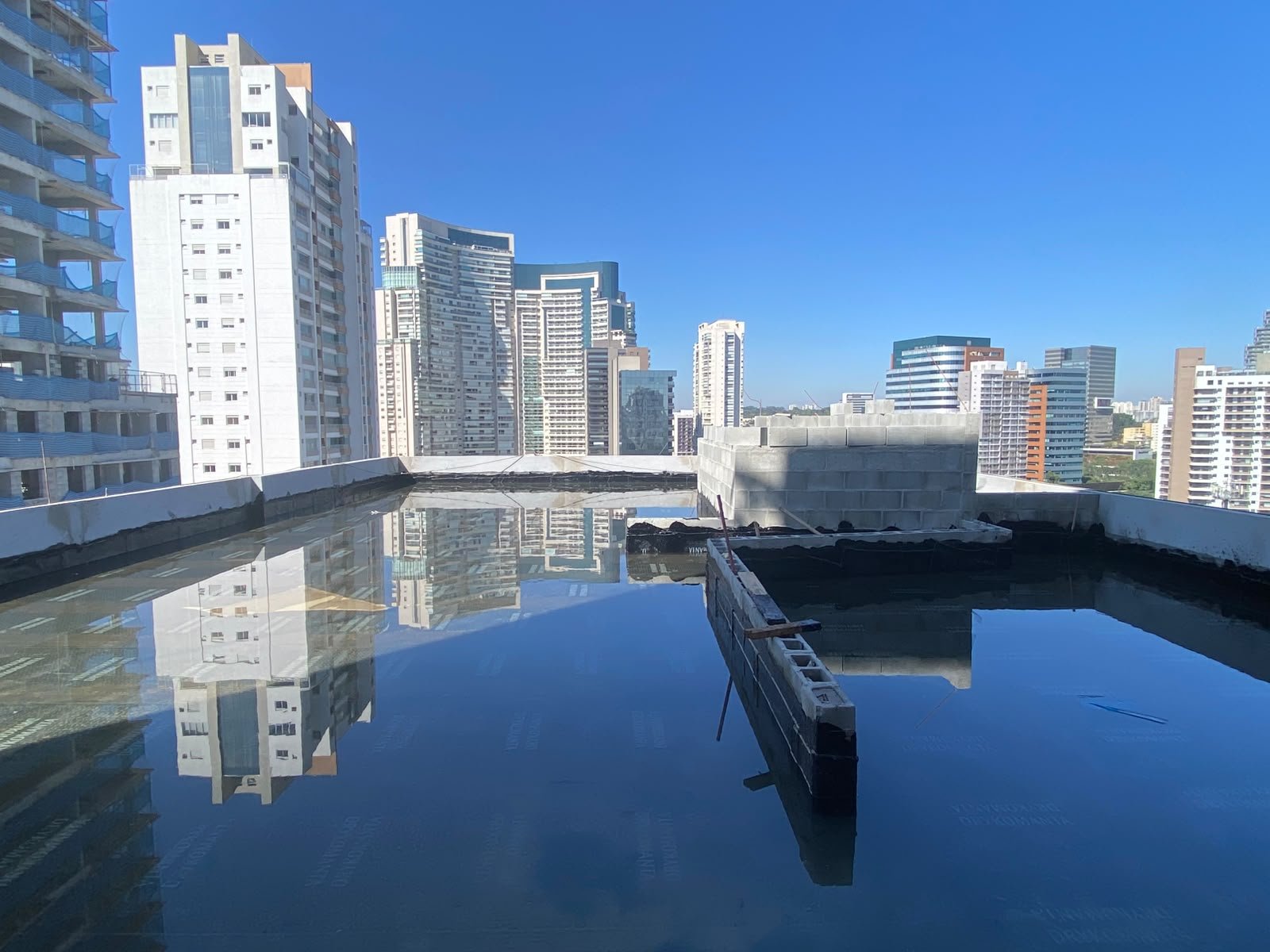 Foto da obra em 28 de setembro de 2026: laje do rooftop em teste de estanqueidade da impermeabilização, com o skyline de Pinheiros