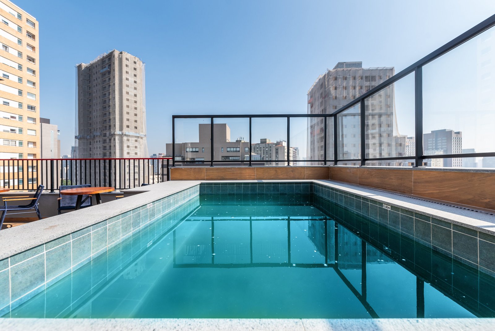 Foto da piscina do rooftop com guarda-corpo de vidro e vista para os prédios de Perdizes