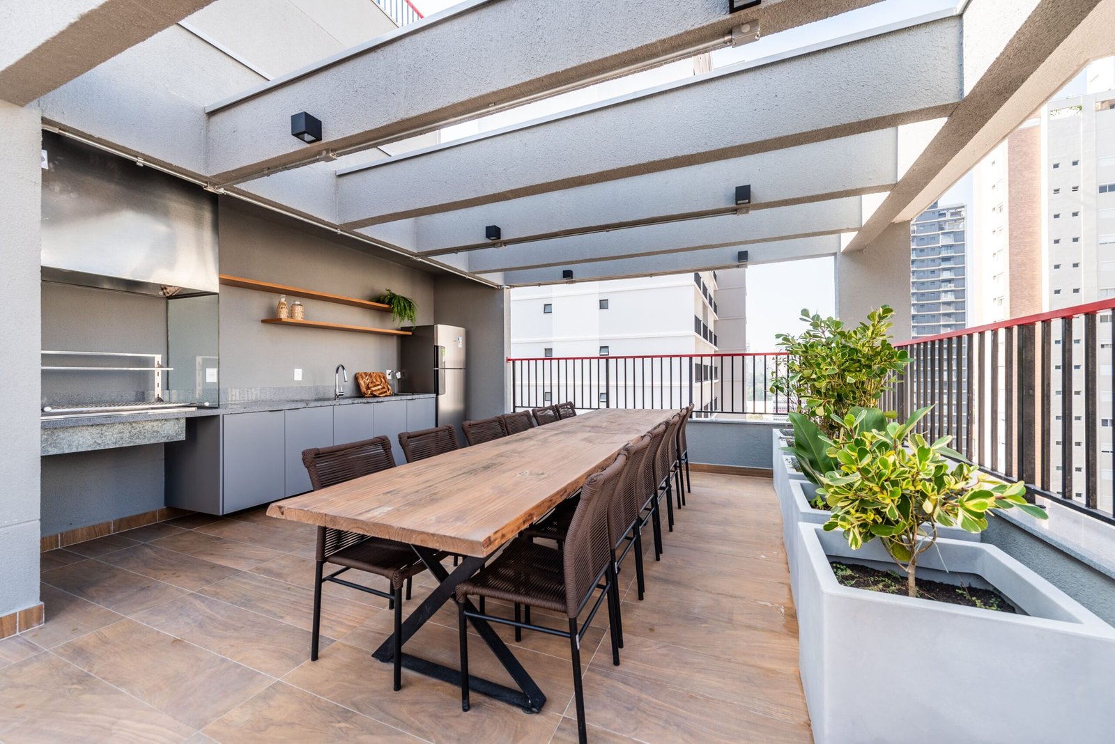 Foto do espaço gourmet do rooftop com churrasqueira, mesa comprida e vista para os prédios de Perdizes