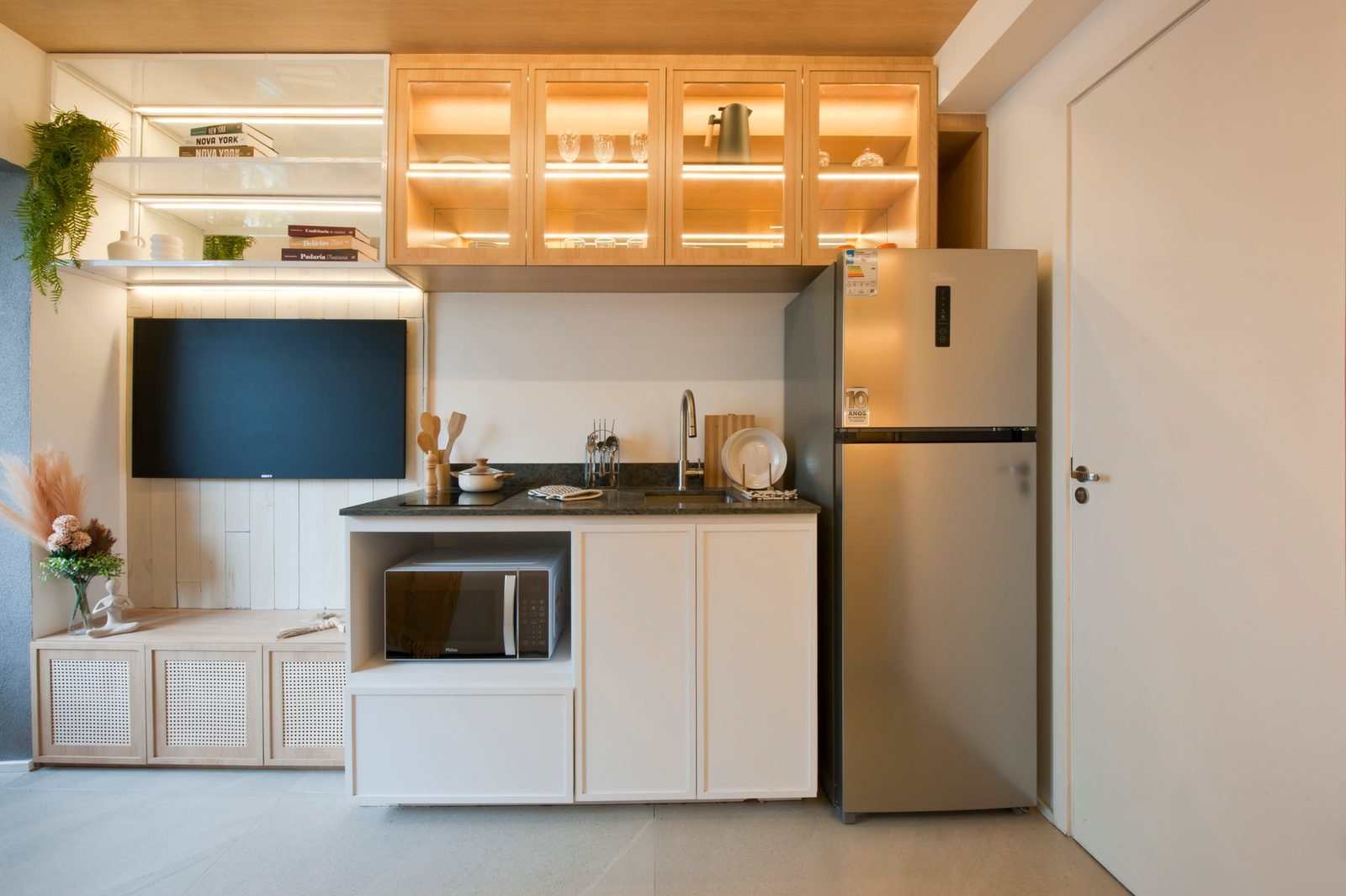 Foto do apartamento decorado de 1 dormitório: cozinha planejada com armários iluminados, TV e geladeira